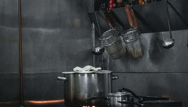 Cocina industrial de acero inoxidable con ollas y utensilios colgados