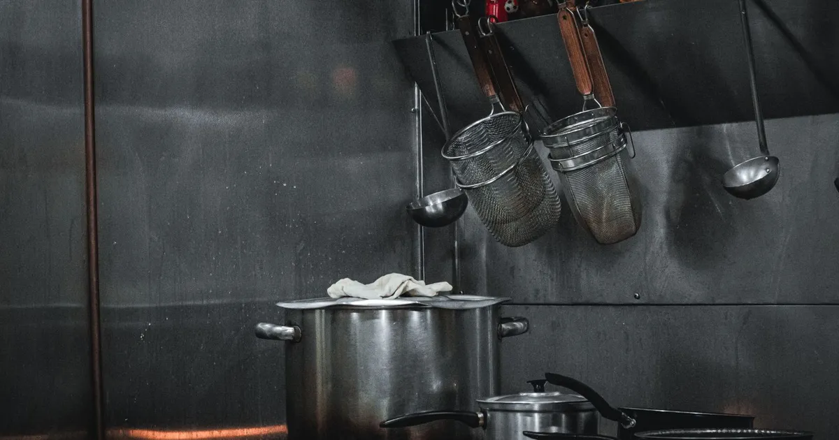 Cocina industrial de acero inoxidable con ollas y utensilios colgados