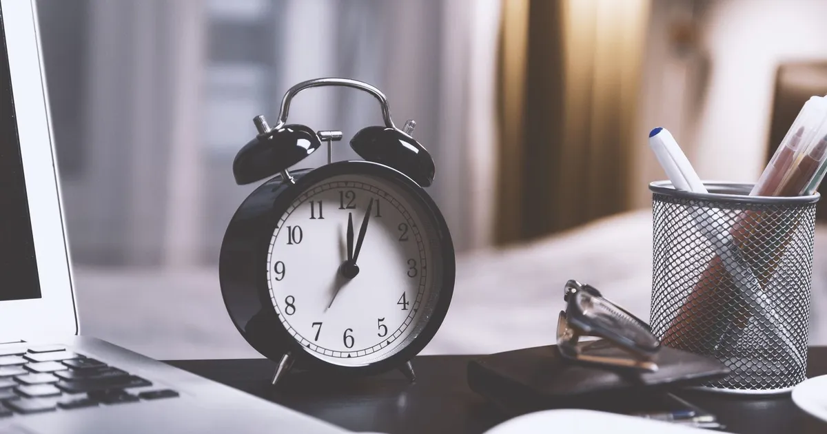 Reloj despertador junto a una laptop en un escritorio de oficina