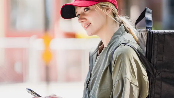 Repartidor con mochila revisando su teléfono en la calle