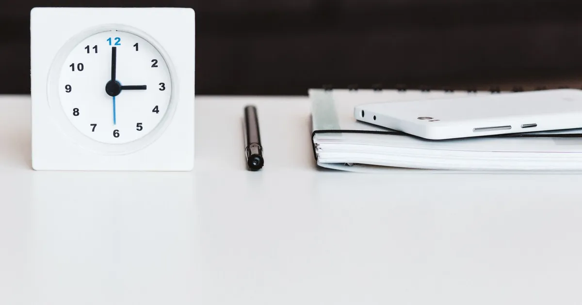 Reloj de escritorio blanco junto a una libreta y un bolígrafo