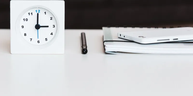 Reloj de escritorio blanco junto a una libreta y un bolígrafo