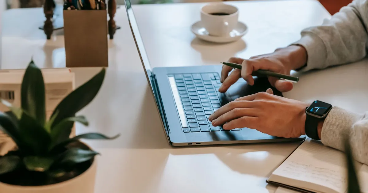 Persona trabajando desde casa en una laptop junto a una taza de café y una libreta
