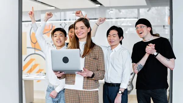 Equipo de trabajo celebrando un logro frente a una laptop en la oficina