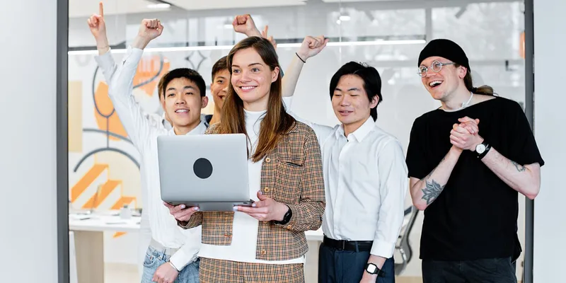 Equipo de trabajo celebrando un logro frente a una laptop en la oficina