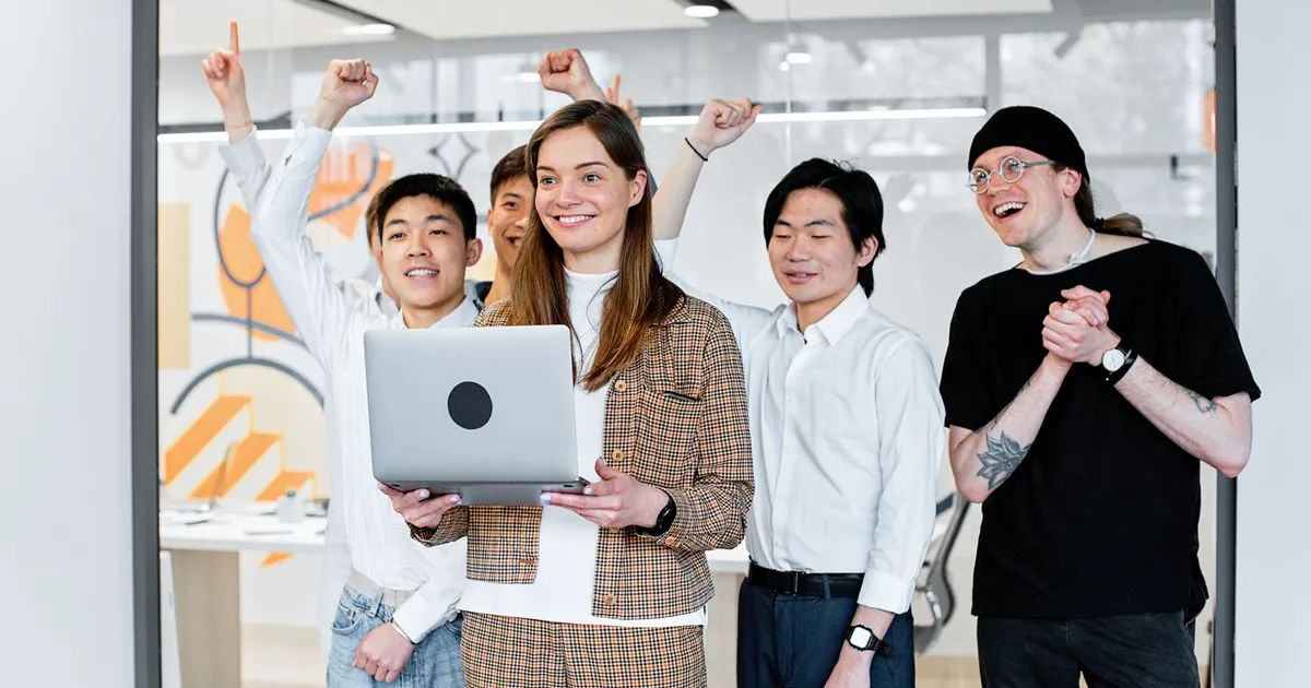 Equipo de trabajo celebrando un logro frente a una laptop en la oficina