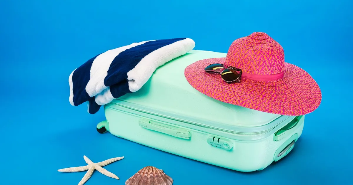 Maleta abierta con sombrero, toalla y artículos de playa listos para vacacionar